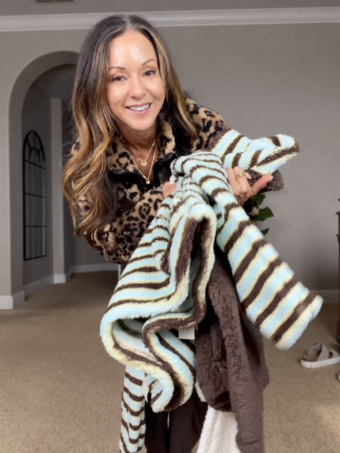 Holly holding several soft, striped plush pullovers in different colors and patterns, highlighting affordable fall and winter layers.